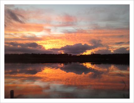 This is a picture of the sunset reflecting over water from a lake.