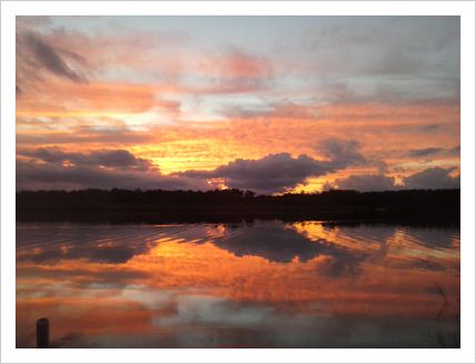 This is a picture of the sunset reflecting over water from a lake.