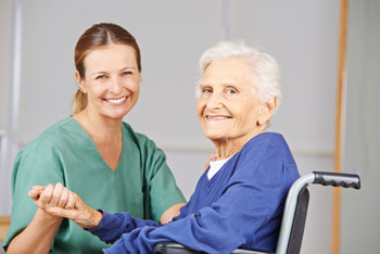 Geriatric nurse and senior woman in wheelchair smiling together in nursing home